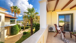 A balcony with a view of a garden, a chair, and a table.