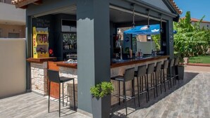 An outdoor bar area with a stone wall, a tiled roof, and a blue umbrella.