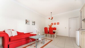 A modern living room with a red sofa, a glass coffee table, and a dining area with red chairs.