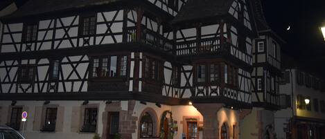 A traditional half-timbered building with a courtyard, a sign indicating a no parking zone, and a car parked outside.