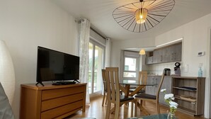 Una sala de estar moderna con televisor de pantalla plana, muebles de madera, una mesa de centro de vidrio y un comedor con sillas.