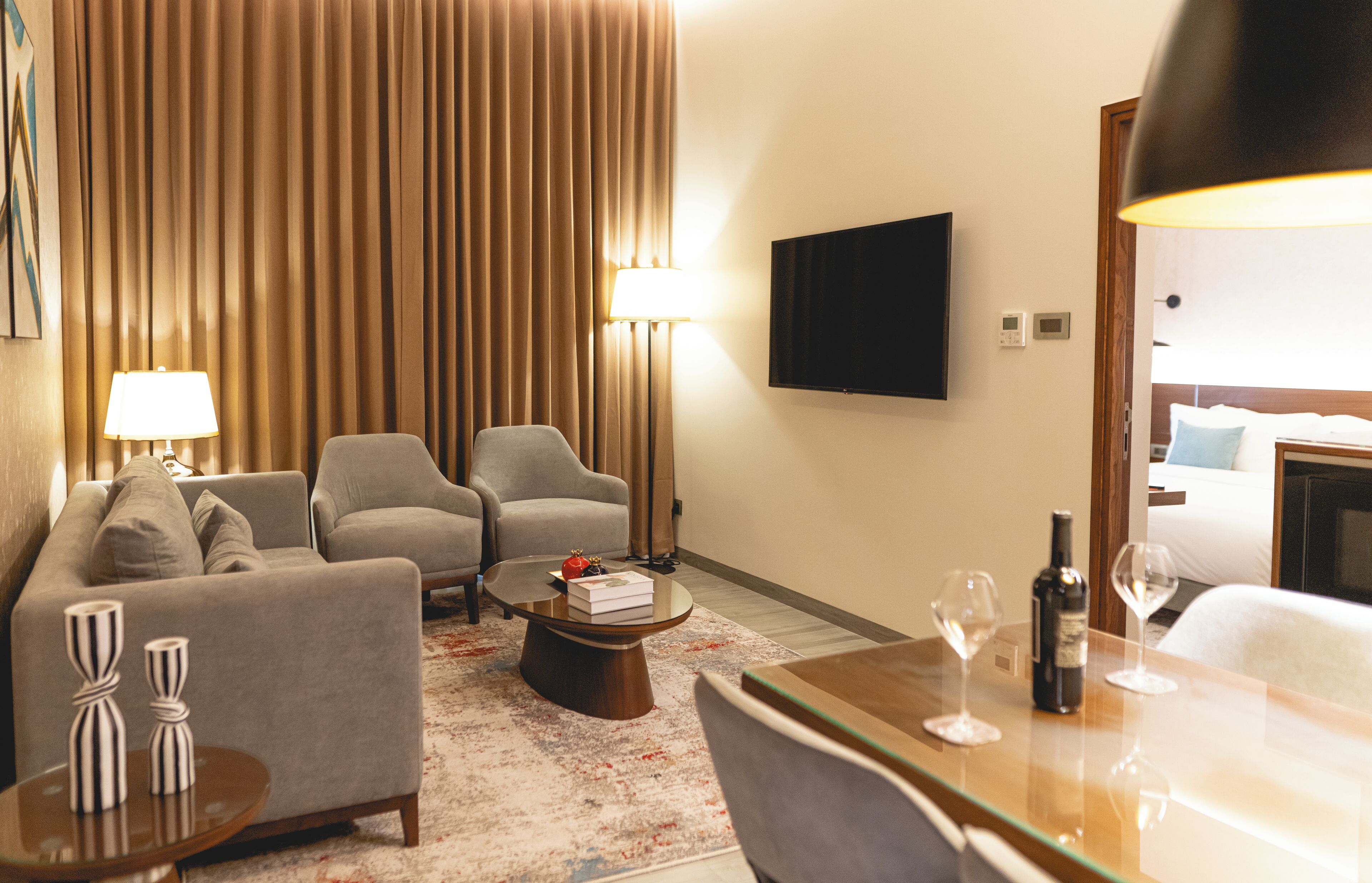 A hotel room with a sofa, two armchairs, a coffee table, a TV, and a bed.