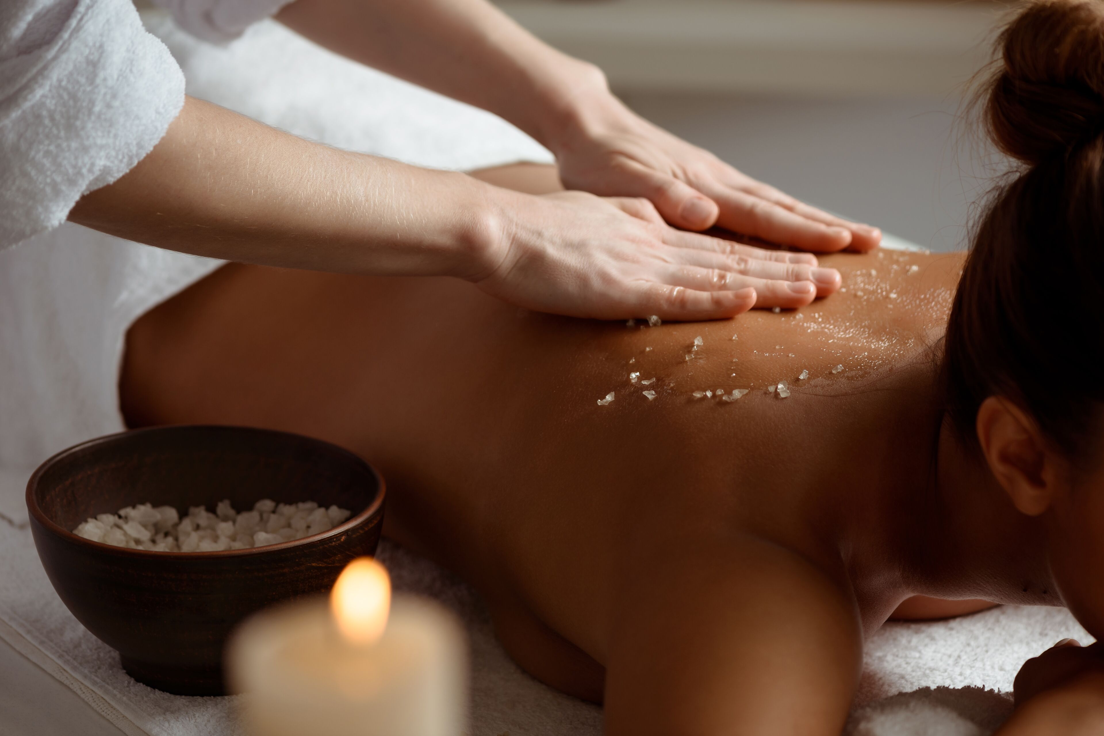 A person receiving a massage with a bowl of salt nearby.