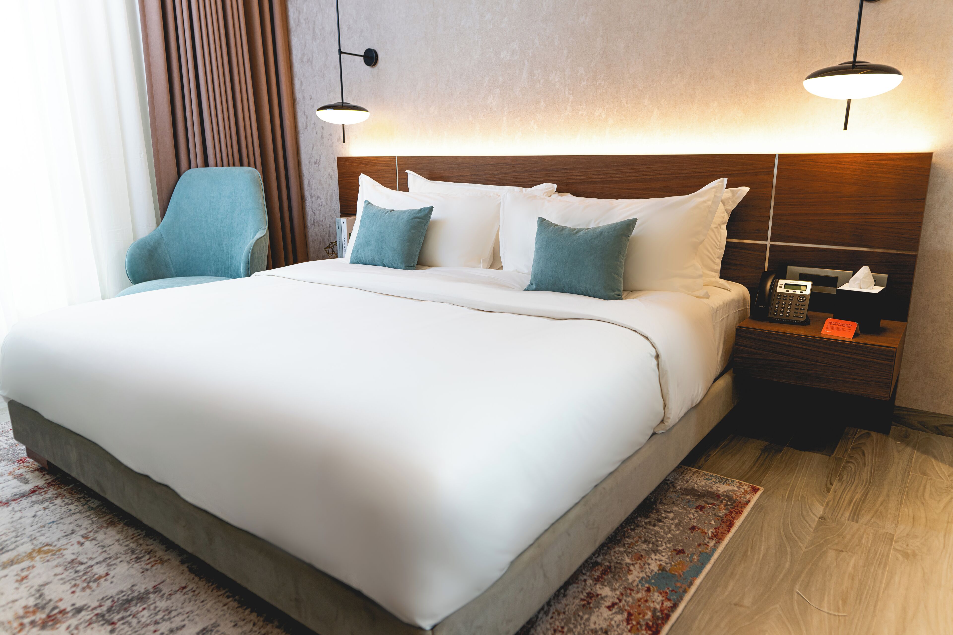 A hotel room with a large bed, two bedside tables, a nightstand, a chair, and a wall-mounted telephone.