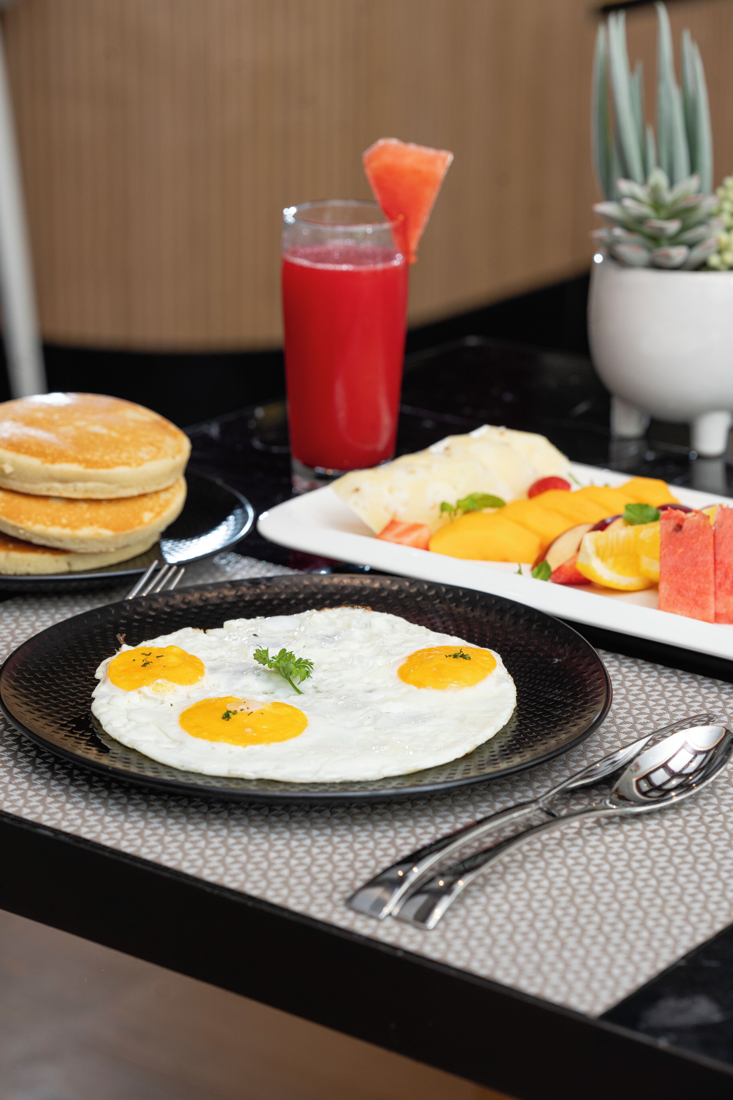 A breakfast setting with pancakes, eggs, fruit, and a smoothie.