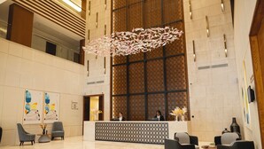 Een ruime lobby met een receptiebalie, zithoek en een grote decoratieve hanglamp.