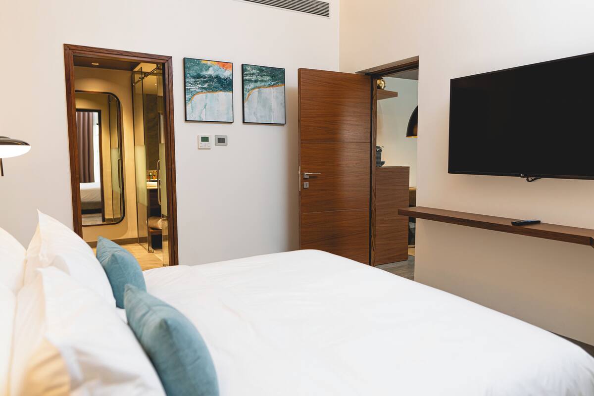 Una habitación de hotel con una cama, un televisor montado en la pared y un armario de madera.
