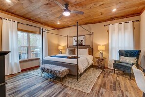 A four-poster bed with a canopy, a chair, a small table, and a window with curtains. - Bucks & Bourbon Lodge 3 King Beds+Hot Tub/Fire Pit (Gilmer County)