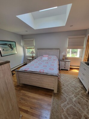 A bedroom with a skylight, a bed with patterned bedding, a nightstand, a dresser, and a framed picture on the wall.