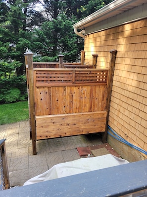 A wooden fence with a lattice design, a wooden bench, and a house with a shingled exterior.