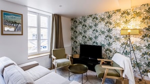Ein Wohnzimmer mit einer Couch, Sesseln, einem Couchtisch, einem Fernseher und einer Wand mit tropischem Wandpapier.