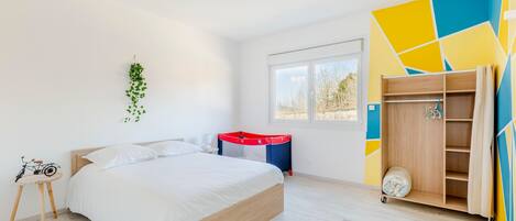 A modern bedroom with a bed, a small table with a bicycle, a wardrobe, and a window with a view.