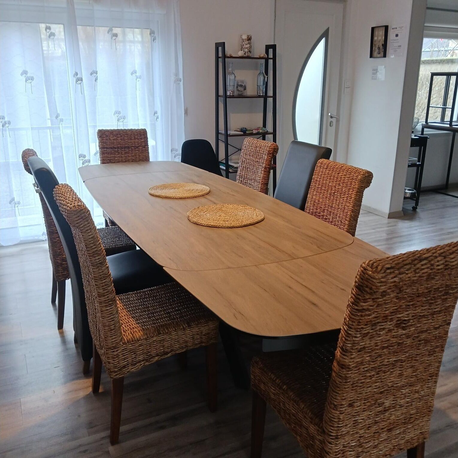 A dining area with a long wooden table, wicker chairs, and two woven placemats.