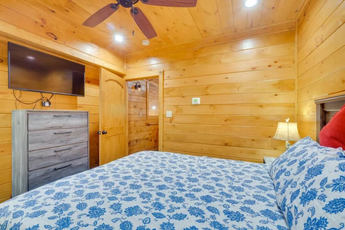 Une chambre dans un chalet en bois, comprenant un lit, une commode, un ventilateur de plafond, une télévision et une lampe.