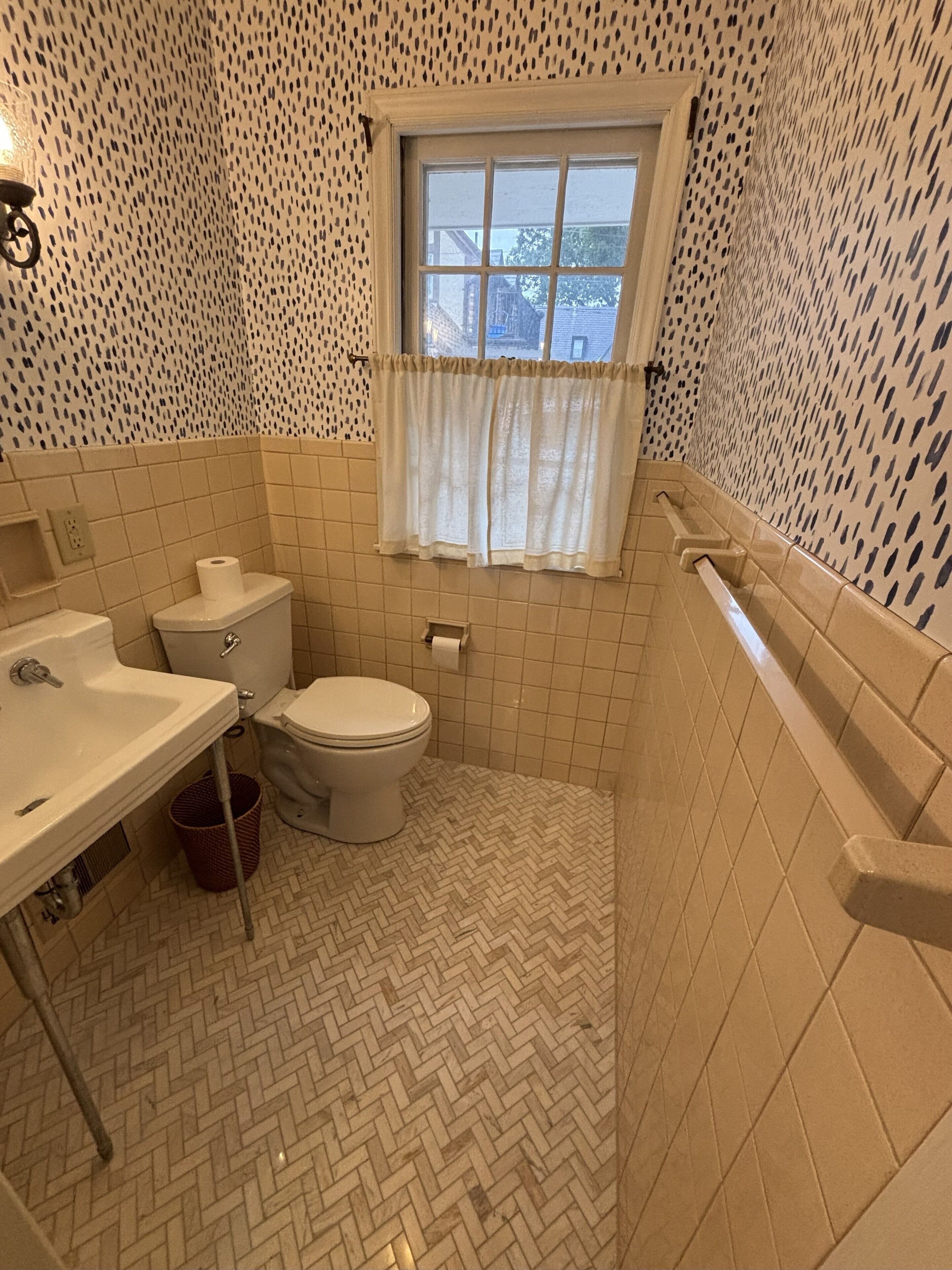 Une salle de bain avec des toilettes, un lavabo et une fenêtre avec un rideau.