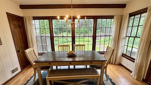 Une salle à manger avec une table en bois, quatre chaises, un lustre et de grandes fenêtres avec des rideaux.