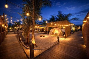Una terraza de madera con una estructura de techo de paja, luces colgantes y palmeras.