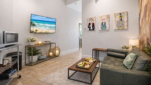 A living room with a flat-screen TV, a leather sofa, a coffee table with fruit, a TV stand with a microwave, and wall art. - Resort Perks: 11 beds, monastery bunks, kitchen (San Diego)