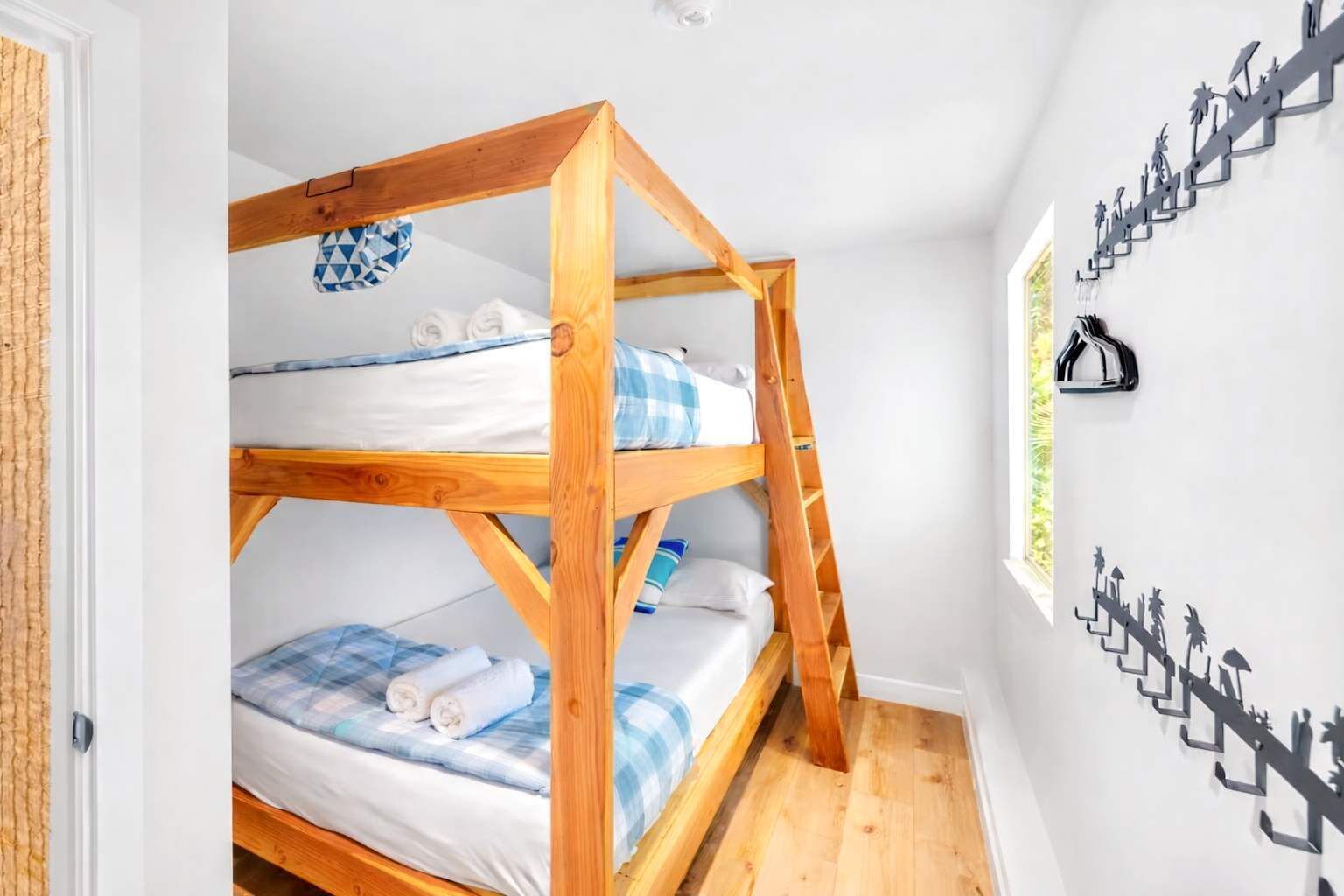 Een slaapkamer met een stapelbed, een houten ladder, witte wanden en een decoratieve wandversiering van mensen die de trap beklimmen.