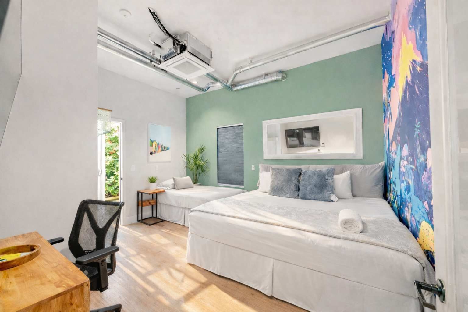Une chambre avec deux lits, un bureau, une chaise et une fenêtre donnant sur un paysage verdoyant.