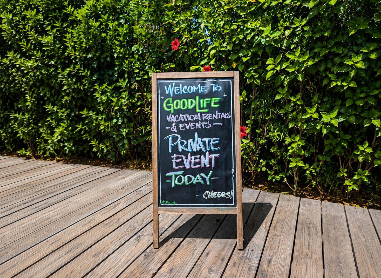 A signboard on a wooden deck with a message welcoming to Goodlife vacation rentals and events, indicating a private event today.