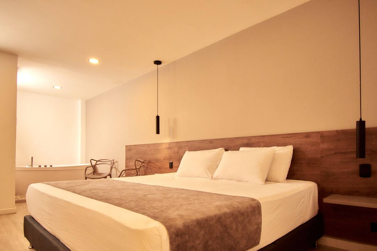 A modern hotel room with a large bed, a wooden headboard, and a minimalist design.