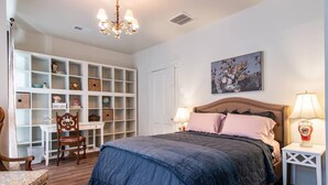 A bedroom with a large bed, a nightstand with a lamp, a chair, a desk, and a shelving unit with various items. - The Gallery Loft - Walk & Dine! (Louisville)
