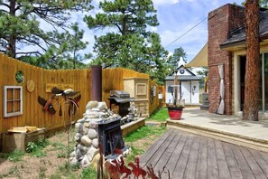 A backyard with a wooden fence, a stone fireplace, a grill, and a small building with a cross on top.