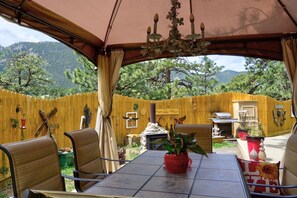 An outdoor patio with a table and chairs, a red potted plant, and a wooden fence. - Pub -  Hot Tub - Fire Pit (Green Mountain Falls)