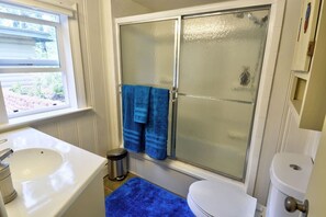 A bathroom with a white sink, a toilet, a shower with frosted glass doors, and a blue bath mat. - Pub -  Hot Tub - Fire Pit (Green Mountain Falls)