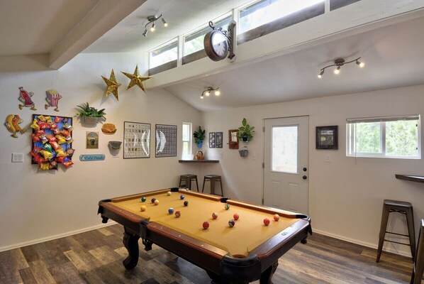 A pool table in a room with a high ceiling, decorative wall art, and a window providing natural light.