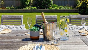 A wooden table set for a meal with a metal champagne bucket, a glass pitcher with lemons, and a potted plant. - Coastal Retreat for 8 with Hot Tub - Walk to Beach (Chichester)