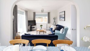 A living room with a TV, sofa, and dining area with chairs and a table. - Coastal Retreat for 8 with Hot Tub - Walk to Beach (Chichester)