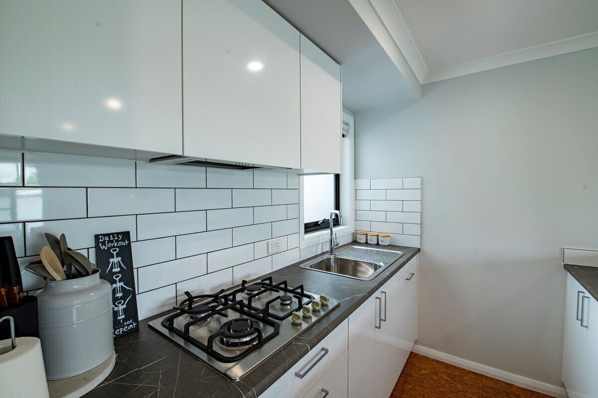 A modern kitchen with white cabinets, a gas stove, a sink, and a chalkboard sign.