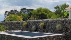 A stone pool surrounded by a stone wall, a grassy area, and a table with a bowl of fruit and a bottle. - Milady, Arcangues vacation rentals (Arcangues)