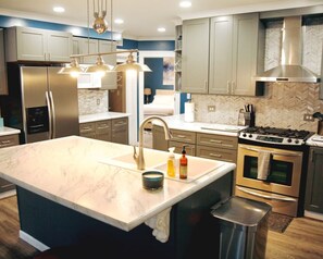 Een moderne keuken met een groot eiland, roestvrijstalen apparatuur en een backsplash van visgraatmozaïek.