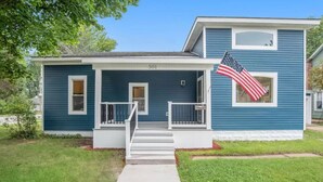 A two-story house with a blue exterior, numbered 501, featuring a front porch with a small set of steps and a railing. - Upscale luxury home just a few blocks from beach (Ludington)