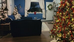 A living room with a blue wall, two Christmas trees, a dark sofa, and a door with a wreath. - Upscale luxury home just a few blocks from beach (Ludington)