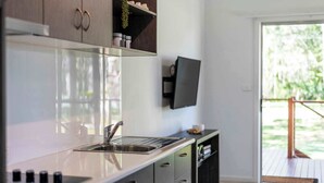 A modern kitchen with a stainless steel sink, a flat-screen TV mounted above it, and a sliding door leading to an outdoor area.