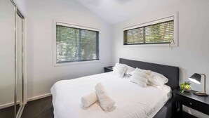 Une chambre d’hôtel avec un lit, des tables de chevet, une lampe et des fenêtres équipées de stores.