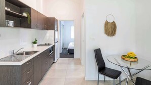 Une cuisine moderne avec des meubles de couleur sombre, un évier en acier inoxydable et une table à manger en verre accompagnée d’une chaise.