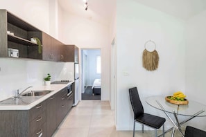 A modern kitchen with dark cabinets, a stainless steel sink, and a glass dining table with a chair. - Lazy Woods Two - Oceanstays (Yamba)