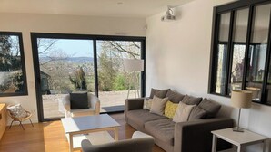 A modern living room with a sofa, coffee table, and a view of a deck and landscape.