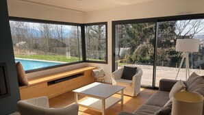 A modern living room with a large window, a pool view, and a cozy seating area.
