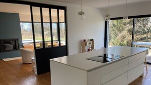 A modern kitchen with a large island, wooden flooring, and a sliding glass door leading to a balcony.