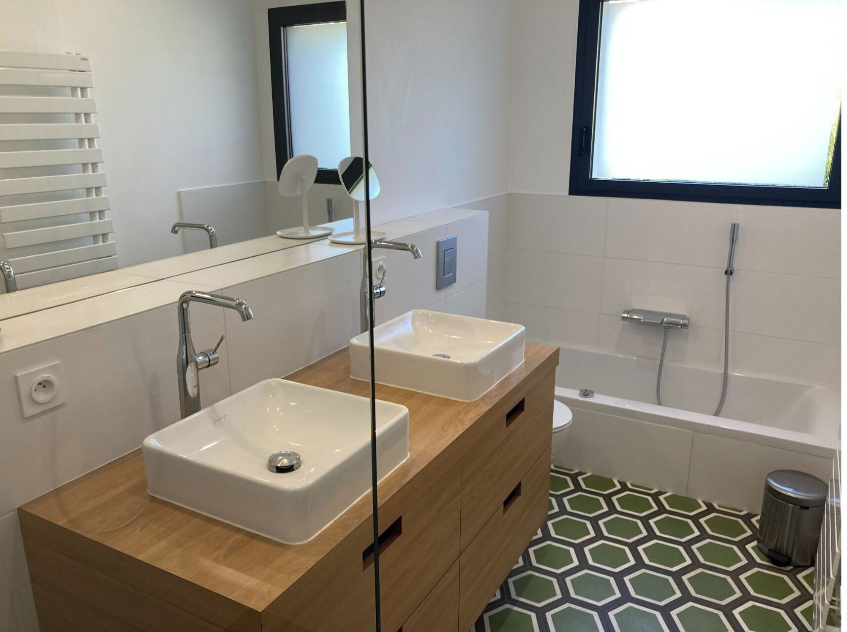 A modern bathroom with two sinks, a mirror, a window, and a bathtub.