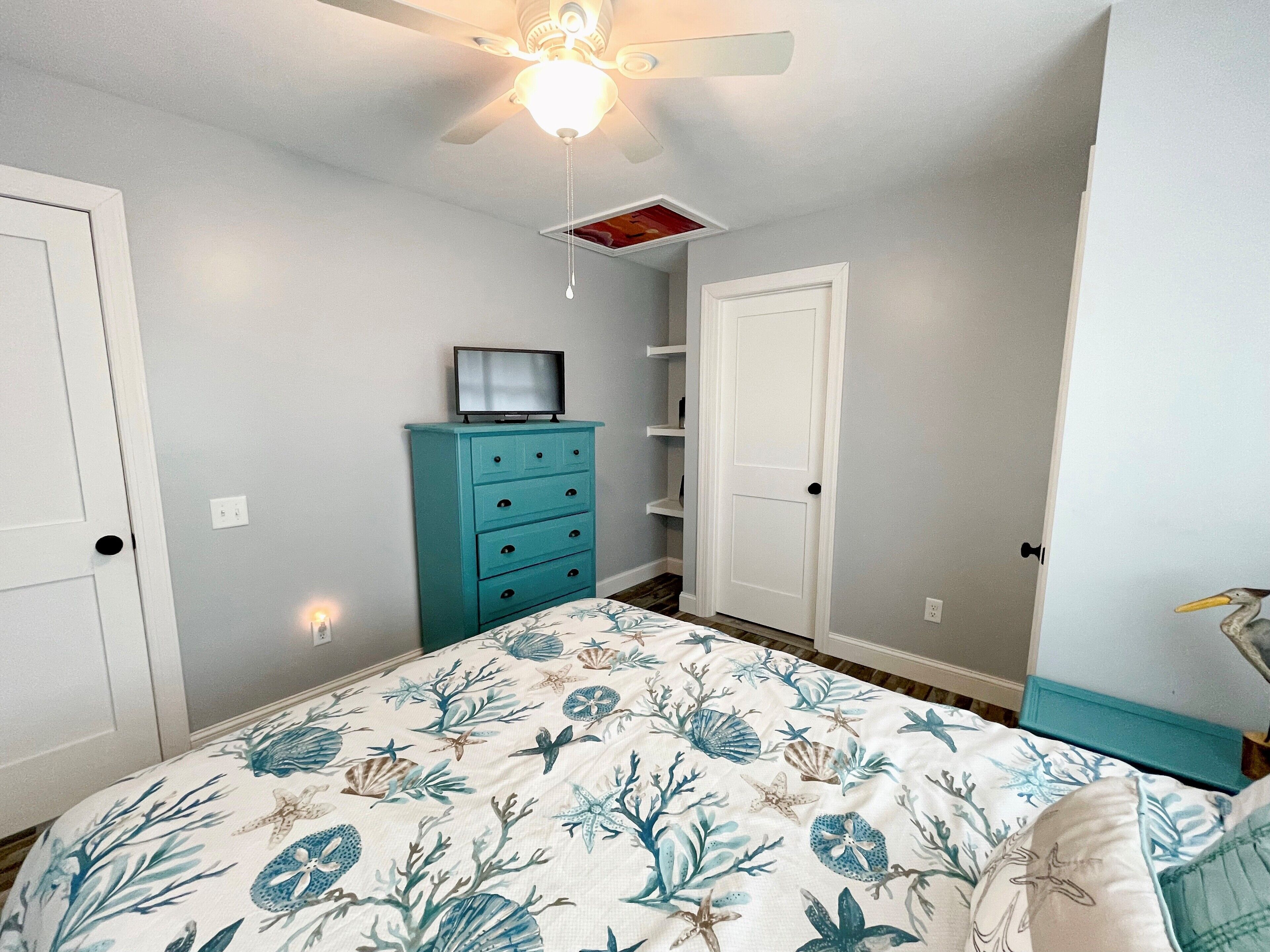 Une chambre à coucher avec un lit, un ventilateur de plafond, une commode et une porte.