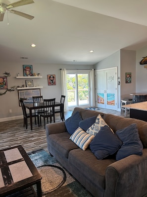 A living room with a brown sofa, a dining table, chairs, a ceiling fan, and artwork on the walls.