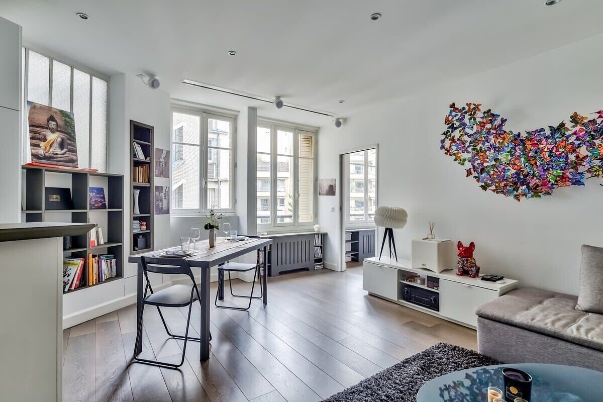A modern living room with a dining area, large windows, and a colorful abstract art piece on the wall.