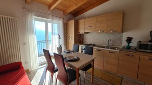 Une cuisine avec des meubles en bois, une table à manger avec des chaises, et une vue sur la mer par une grande fenêtre.